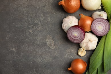 Photo of Fresh whole and cut onions, leek, garlic on grey table, flat lay. Space for text