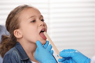 Photo of Doctor examining girl`s oral cavity with tongue depressor indoors. Space for text