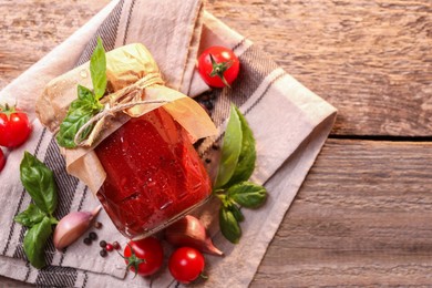 Photo of Jar of tasty tomato paste with water drops and ingredients on wooden table, flat lay. Space for text