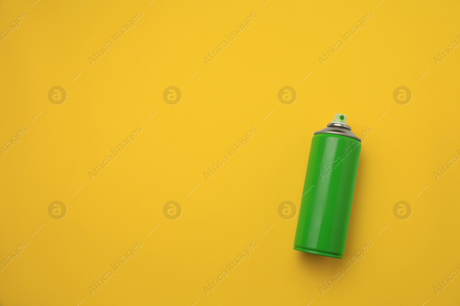 Photo of Can of green graffiti spray paint on yellow background, top view. Space for text