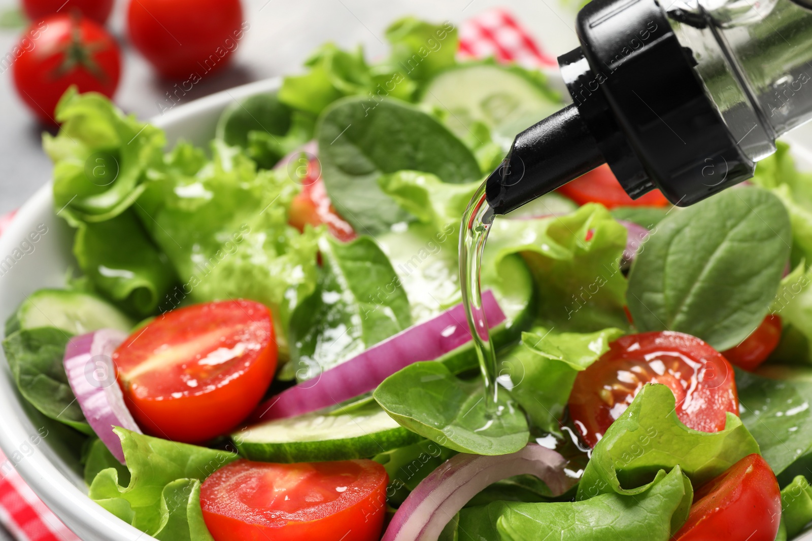 Photo of Pouring oil into delicious vegetable salad in white bowl, closeup