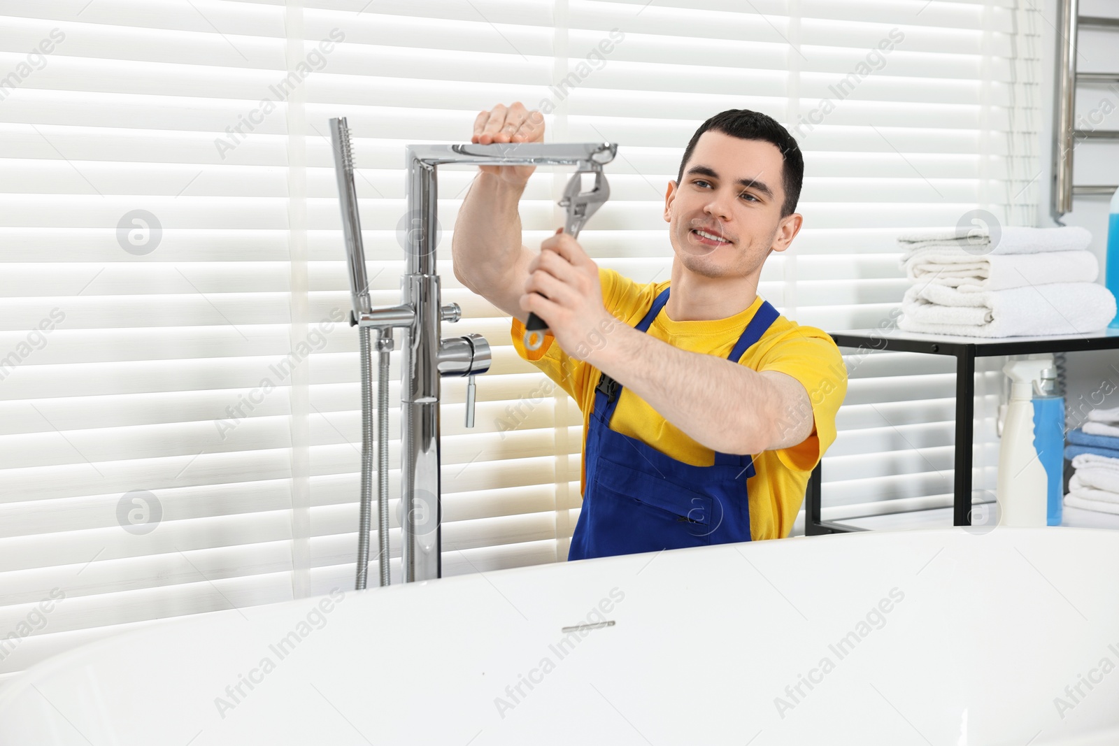 Photo of Smiling plumber repairing faucet with spanner in bathroom