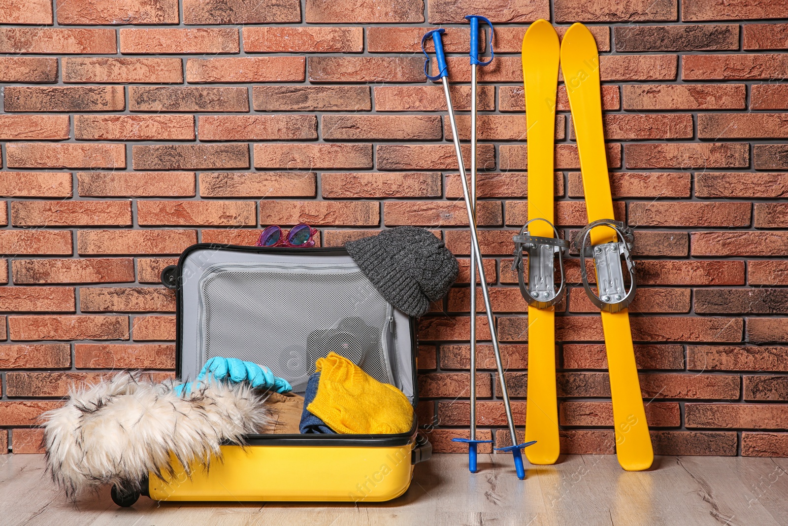 Photo of Suitcase with clothes, camera and skis on floor against brick wall. Winter vacation