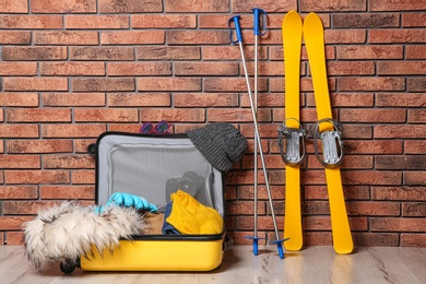 Suitcase with clothes, camera and skis on floor against brick wall. Winter vacation