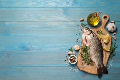 Fresh raw crucian carp and ingredients on light blue wooden table, flat lay with space for text. River fish