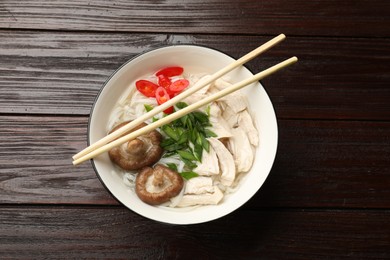 Photo of Delicious ramen with meat in bowl and chopsticks on wooden table, top view. Noodle soup