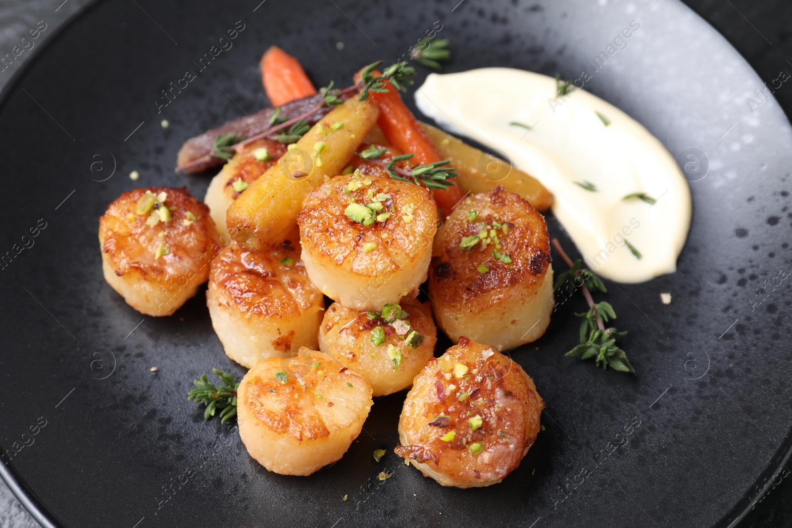 Photo of Delicious fried scallops with carrot and spices on dark gray plate, closeup