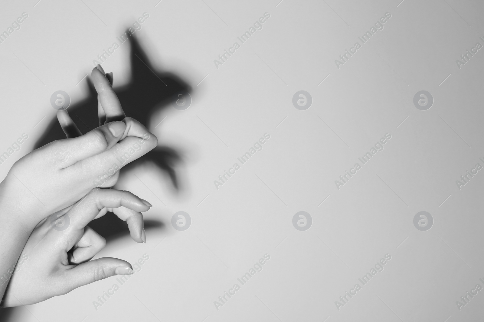 Photo of Shadow puppet. Woman making hand gesture like rabbit on light background, closeup with space for text. Black and white effect