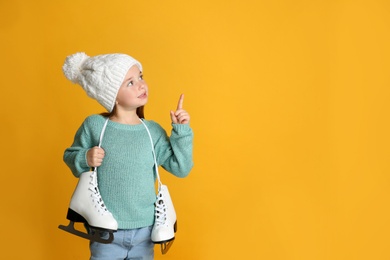 Cute little girl in turquoise knitted sweater with skates on yellow background, space for text