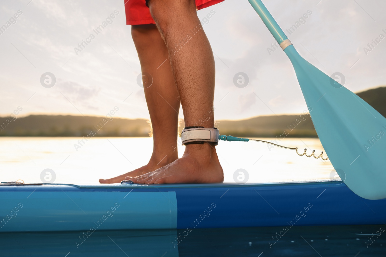 Photo of Man paddle boarding on SUP board in river at sunset, closeup