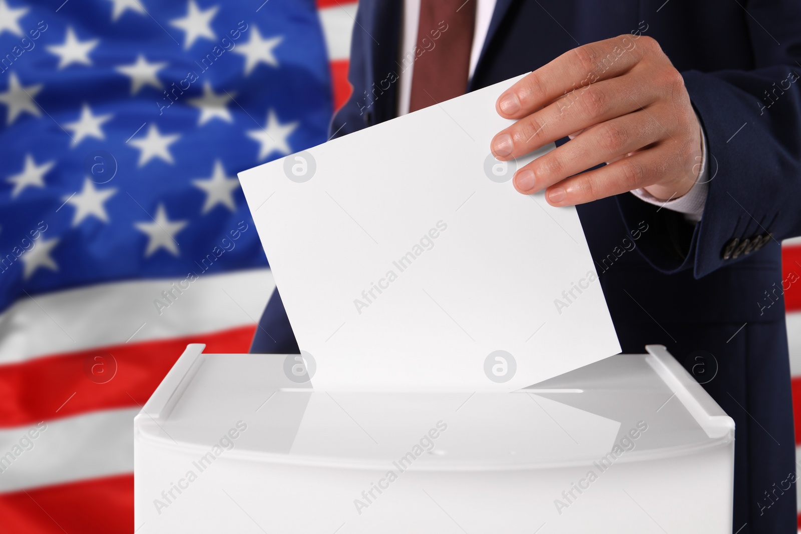 Image of Man putting his vote into ballot box against national flag of United States, closeup