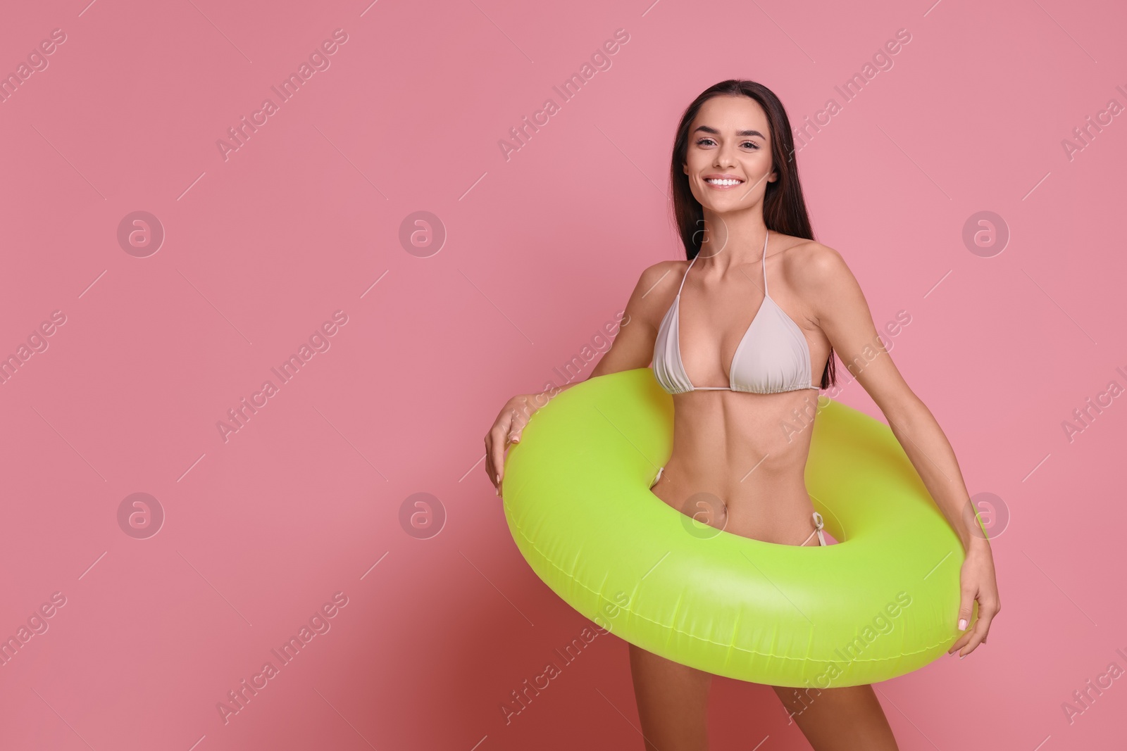 Photo of Young woman in stylish bikini with inflatable ring on pink background, space for text