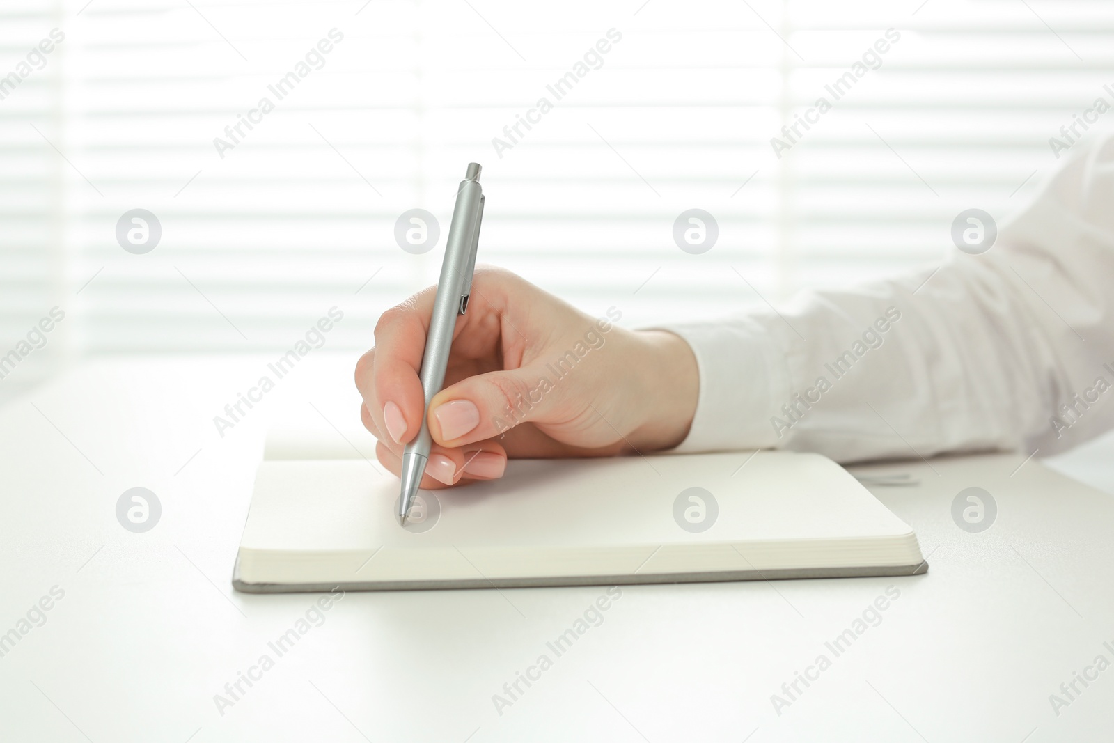 Photo of Woman writing in notebook at white table, closeup