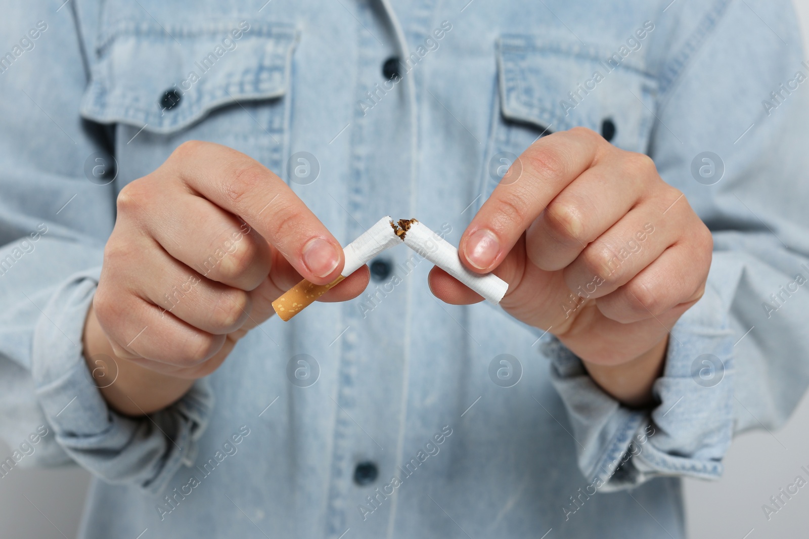 Photo of Stop smoking concept. Woman breaking cigarette on light grey background, closeup