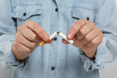 Photo of Stop smoking concept. Woman breaking cigarette on light grey background, closeup