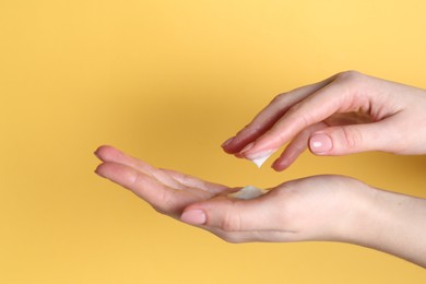 Photo of Woman applying cream on her hand against yellow background, closeup