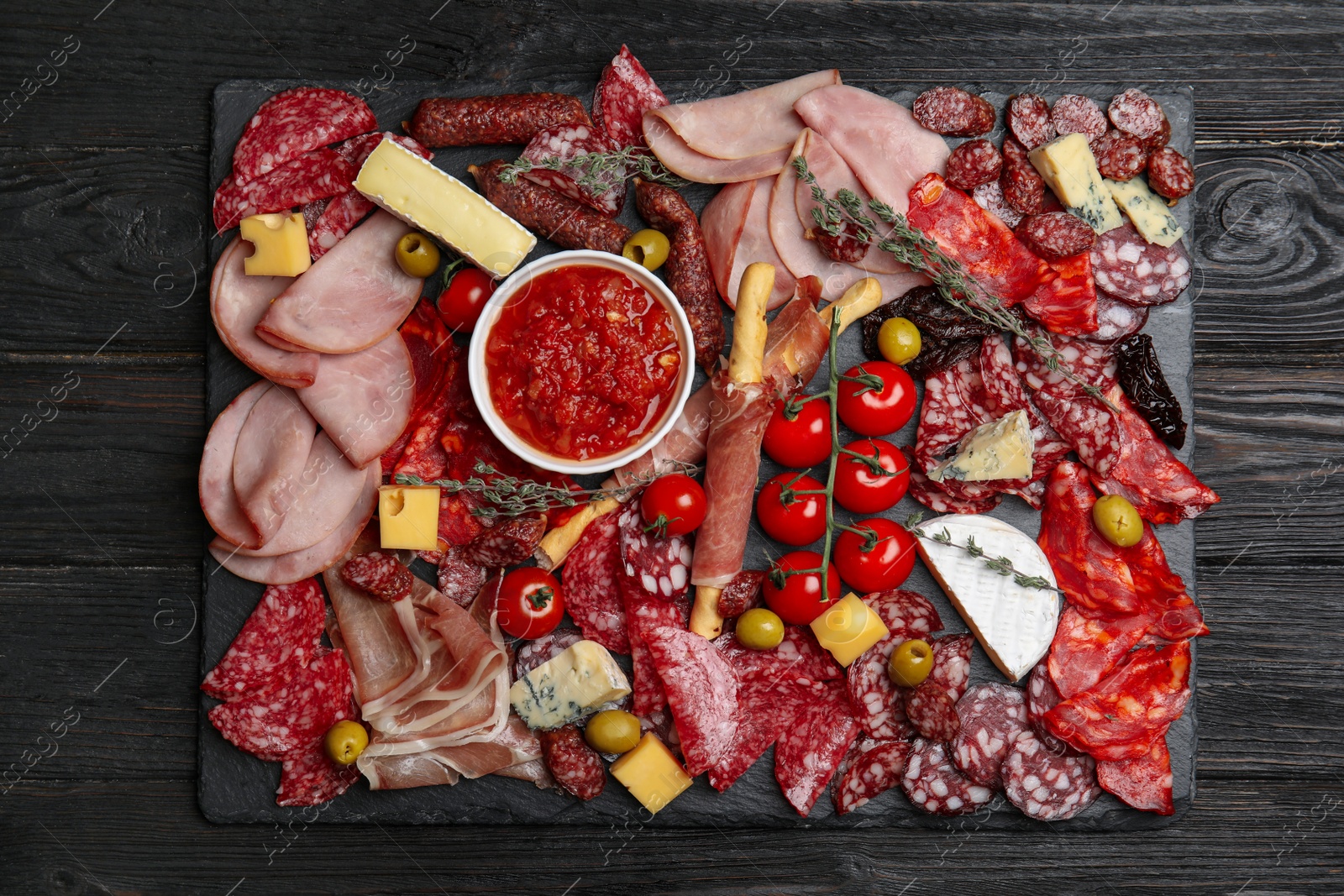 Photo of Tasty ham with other delicacies served on black wooden table, top view