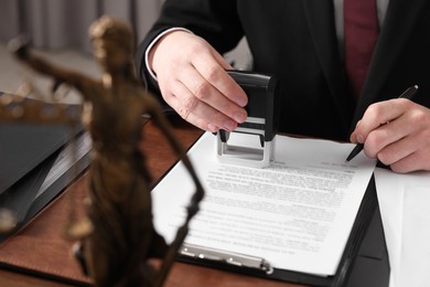 Photo of Notary with pen stamping document at table in office, closeup