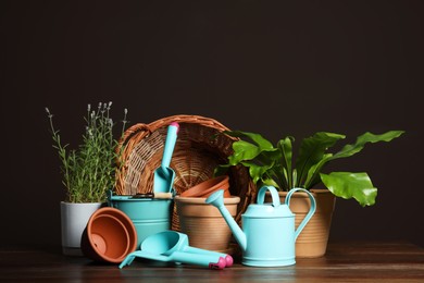 Beautiful plants and gardening tools on wooden table against brown background
