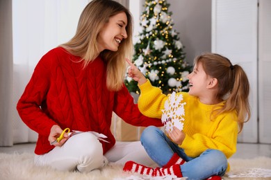 Photo of Happy mother and daughter with paper snowflake near Christmas tree at home