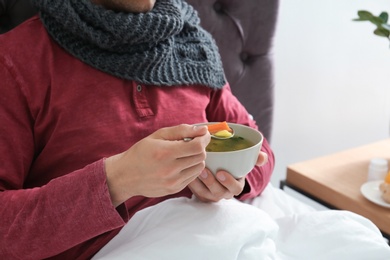 Photo of Sick young man eating broth to cure cold in bed at home