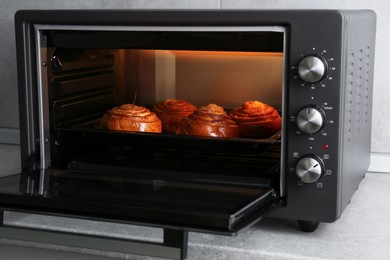 Photo of Open electric oven with delicious pastry on grey table indoors