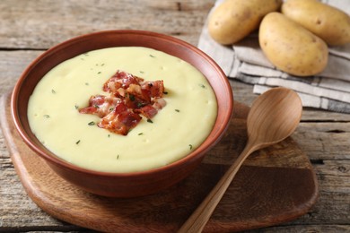 Tasty potato soup with bacon and rosemary in bowl served on wooden table