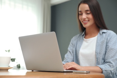 Photo of Young woman using laptop for search at wooden table in room