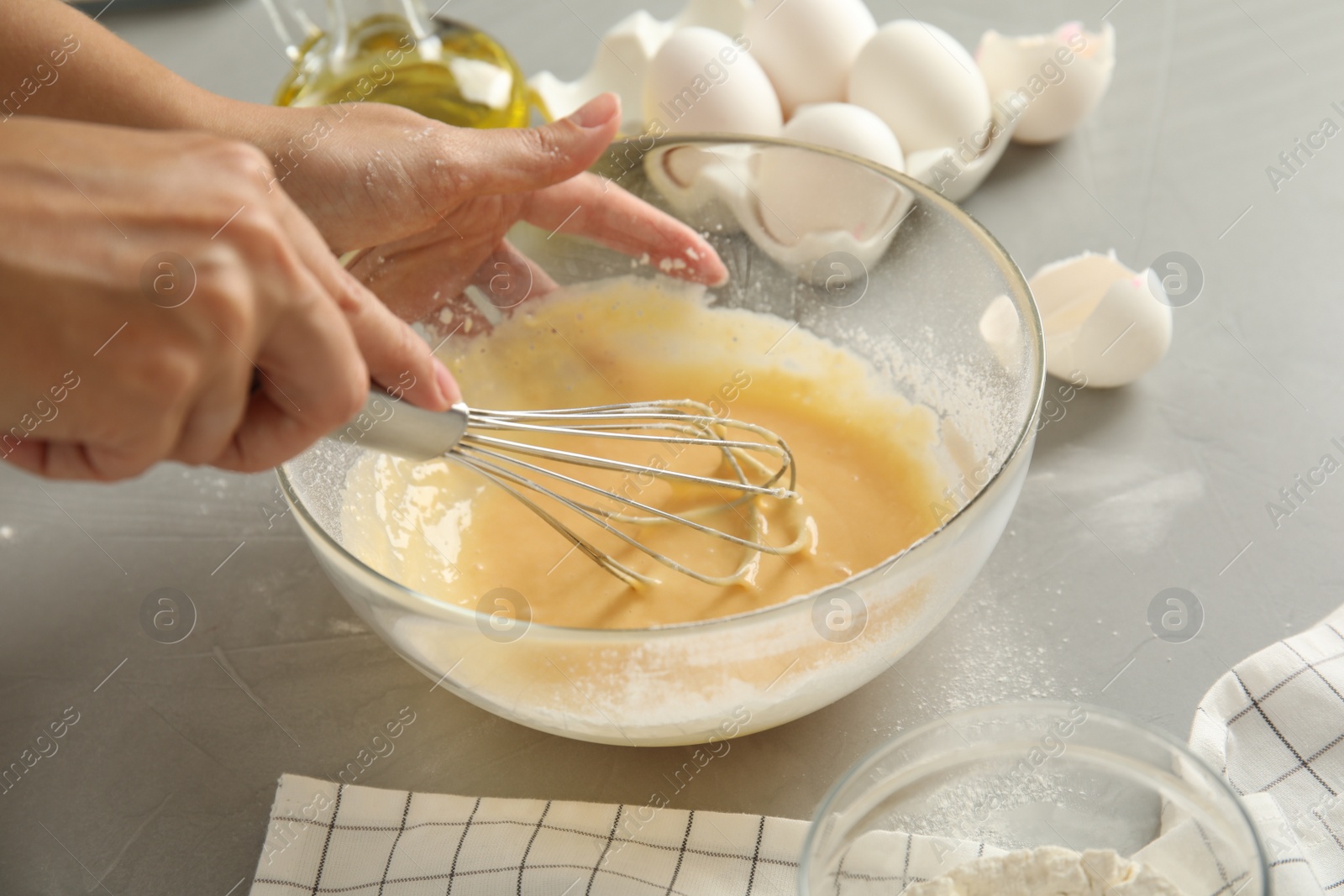 Photo of Woman whisking dough for cake at light grey table, closeup