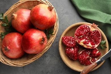 Photo of Fresh pomegranates, green leaves and knife on grey table, top view