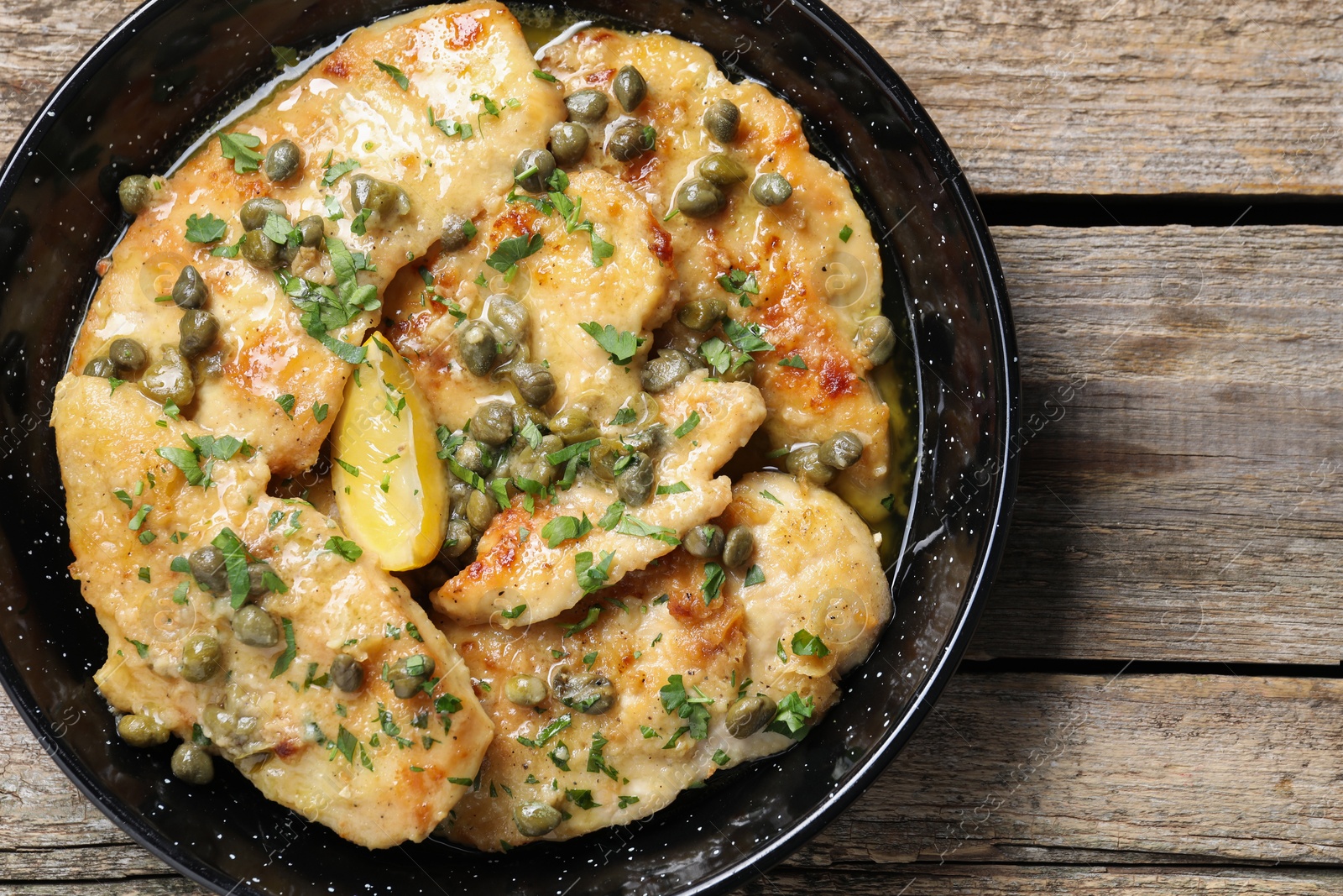 Photo of Delicious chicken piccata with herbs on wooden table, top view