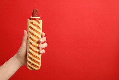 Photo of Woman holding delicious french hot dog on red background, closeup. Space for text