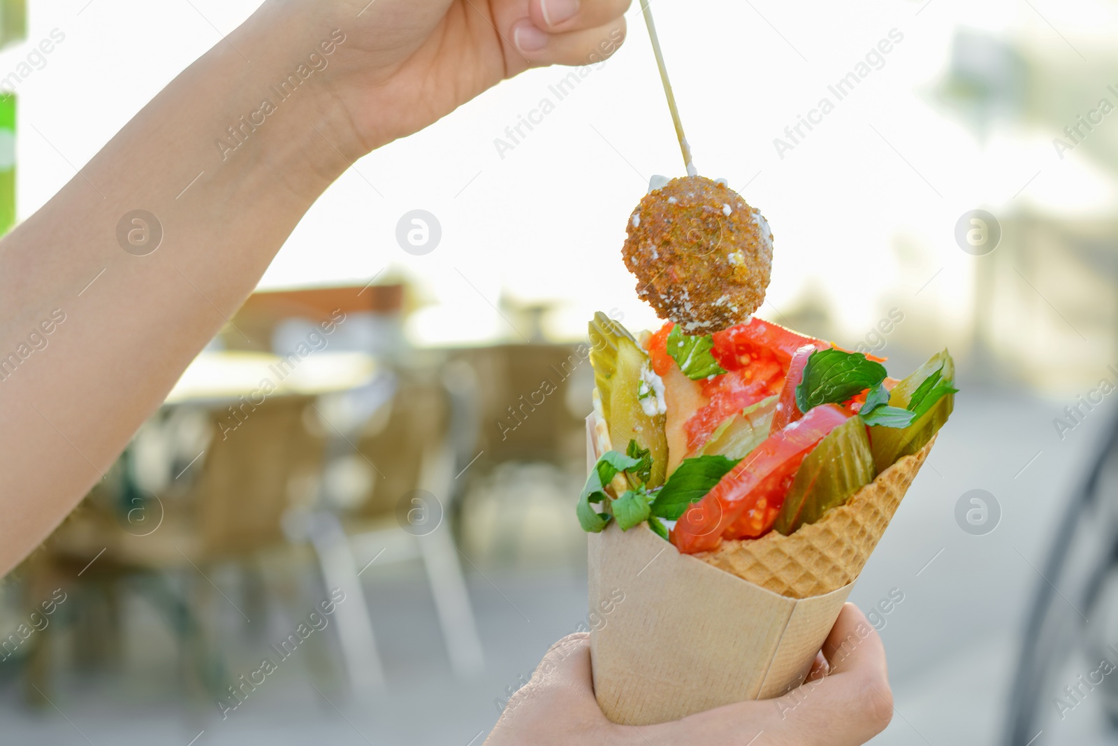 Photo of Woman eating wafer with falafel and vegetables outdoors, closeup. Street food