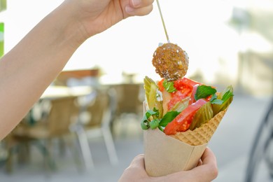 Woman eating wafer with falafel and vegetables outdoors, closeup. Street food