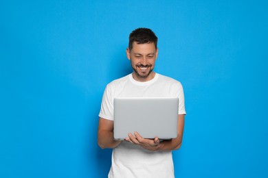 Happy man looking at laptop on light blue background. Space for text