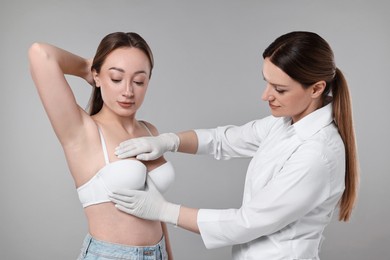 Mammologist checking woman's breast on gray background