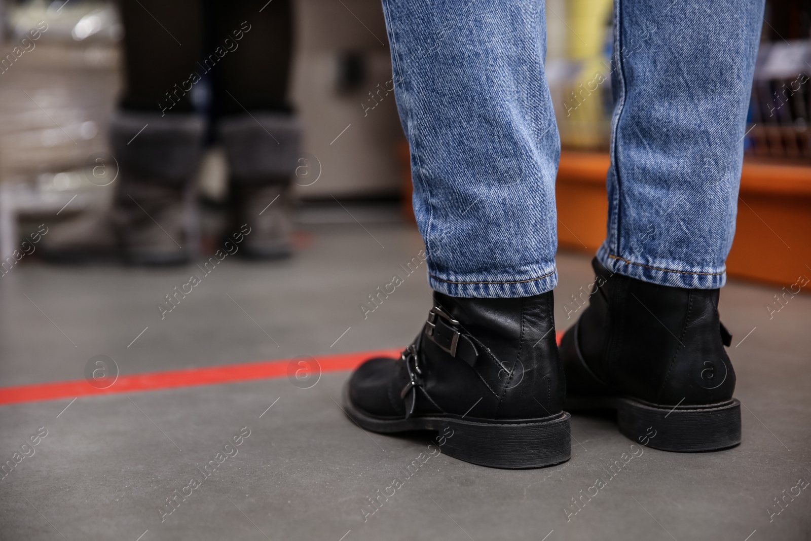 Photo of Person standing behind taped floor marking in line for social distance, closeup. Preventive measure during coronavirus pandemic