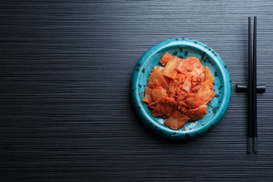 Plate of spicy cabbage kimchi and chopsticks on black wooden table, flat lay. Space for text