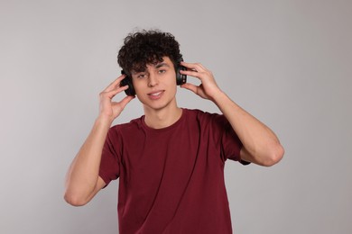 Handsome young man listening to music with headphones on light grey background