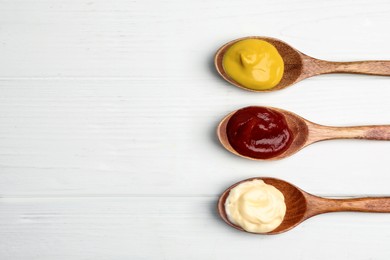Photo of Ketchup, mayonnaise and mustard in spoons on white wooden table, flat lay. Space for text