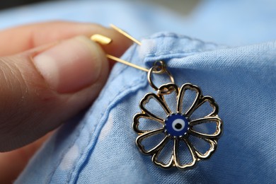 Photo of Woman pinning evil eye amulet on clothing, closeup