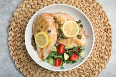 Photo of Delicious cooked chicken fillets with capers and salad on light grey table, top view