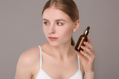 Photo of Beautiful young woman with bottle of essential oil on light grey background