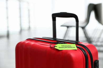 Photo of Red suitcase with TRAVEL INSURANCE label indoors, closeup