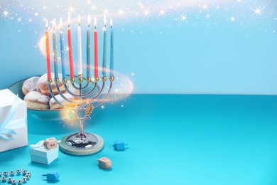 Image of Hanukkah celebration. Menorah with burning candles, dreidels, gift boxes and donuts on light blue table, space for text