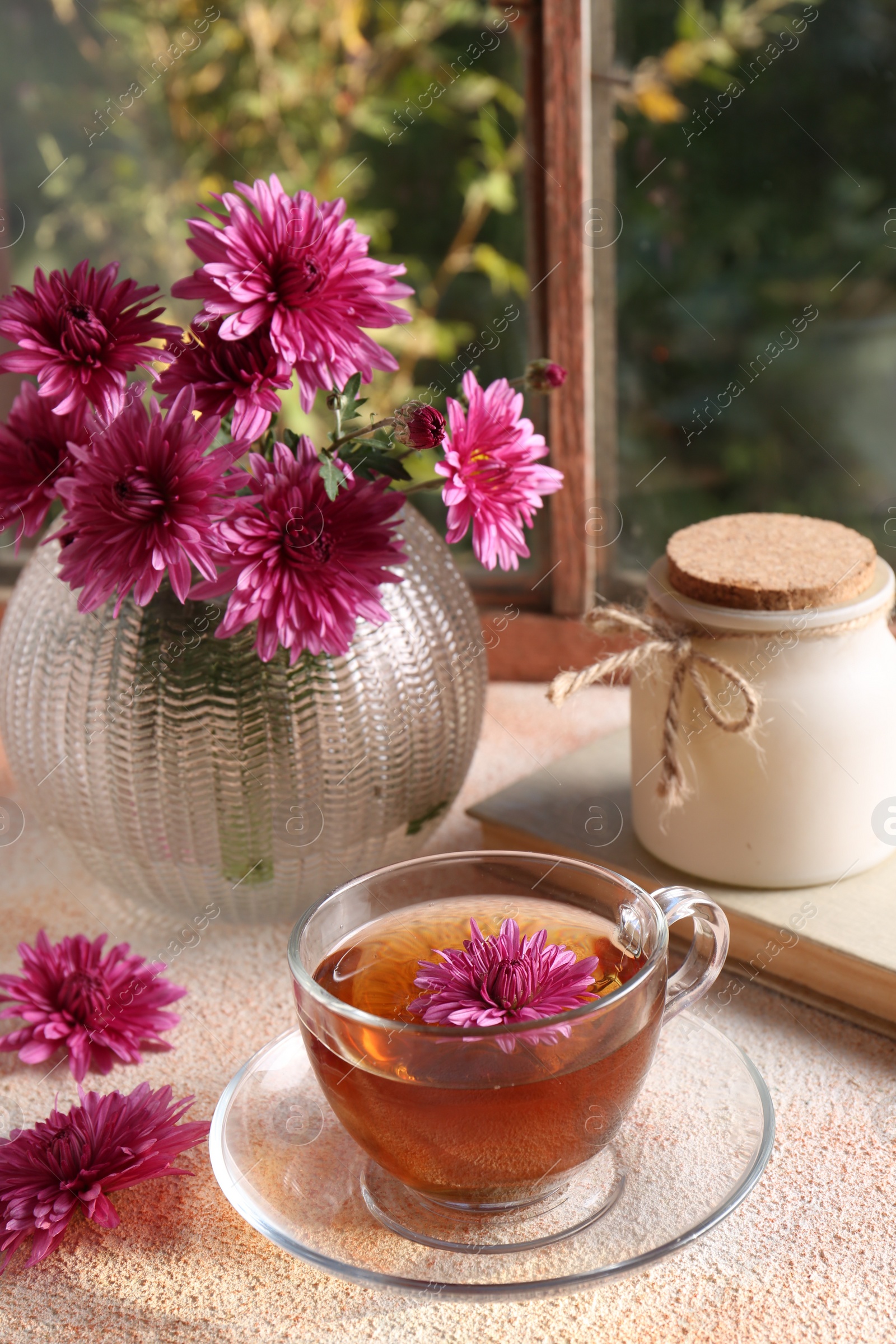 Photo of Beautiful chrysanthemum flowers in vase and cup of tea on beige textured table near window. Autumn still life