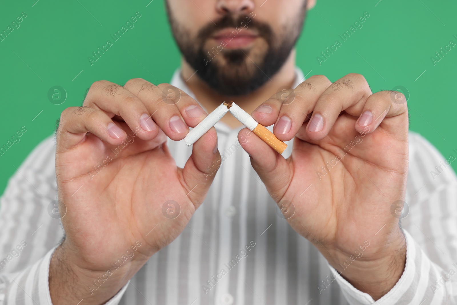 Photo of Stop smoking concept. Man breaking cigarette on green background, closeup