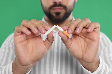 Photo of Stop smoking concept. Man breaking cigarette on green background, closeup