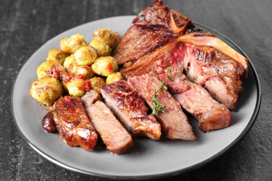 Delicious fried beef meat, vegetables and thyme on black table, closeup