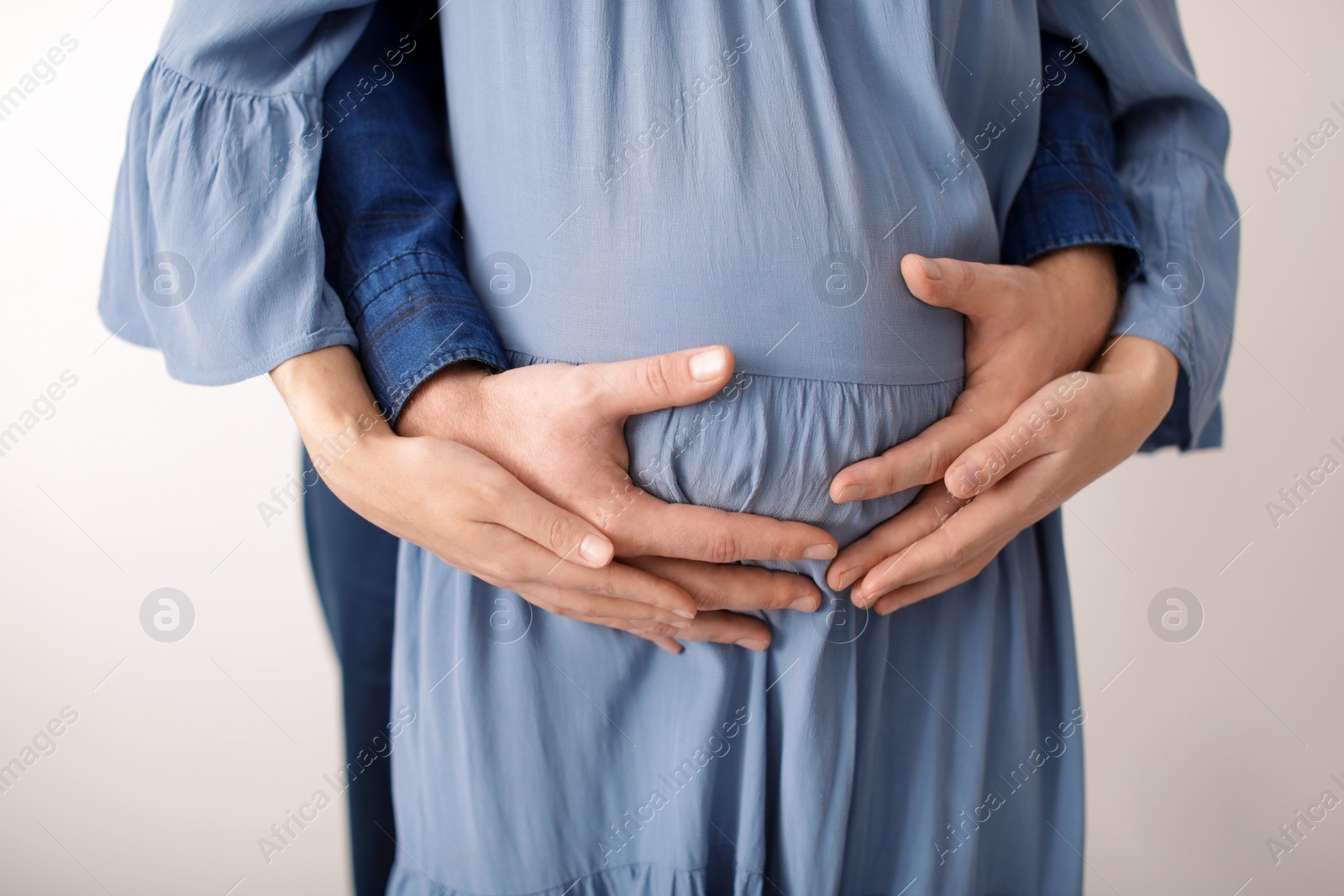 Photo of Young pregnant couple on light background, closeup of hands